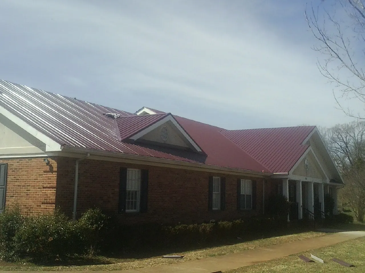 Red metal roof with gabled entries on a long brick building, from a Hail Damage Roof Repair job in Kearsarge