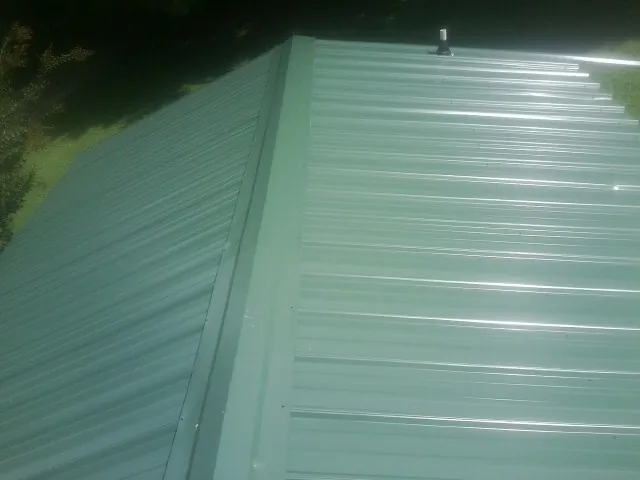 New green metal panels meeting at the ridge of a roof — Flat Roof Repair work by our crew in Kearsarge