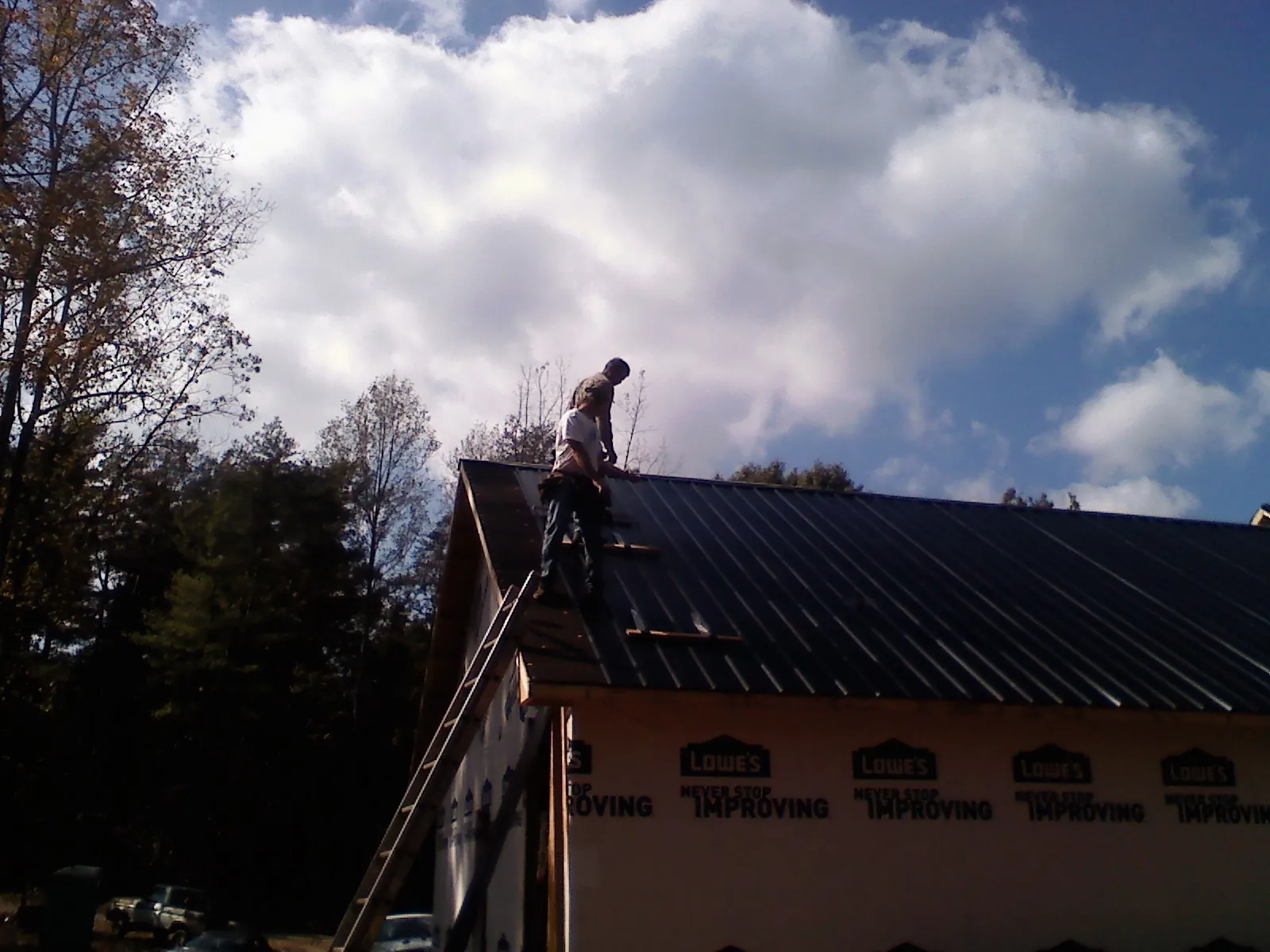 Roofer fastening dark metal panels high against a cloudy sky, from a Roof Inspection job in Kearsarge