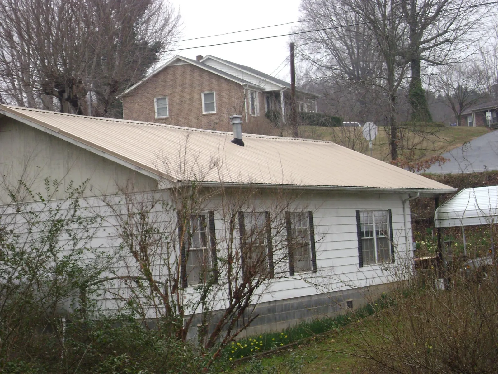 Tan metal roof on a white sided house set into a hillside — Commercial Roofing by Roofing Brothers in Kearsarge