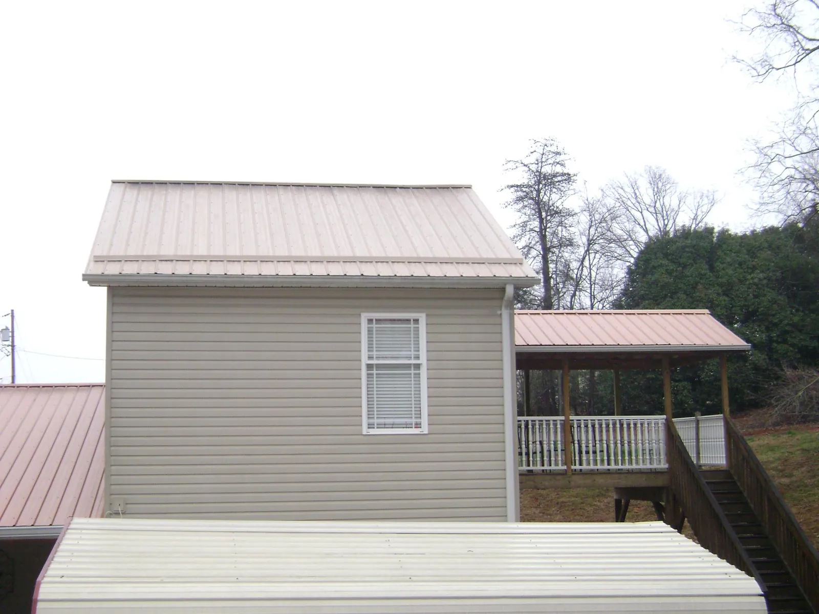 Tan metal roofs on a two story addition and attached porch, from a Roof Replacement job in Kearsarge